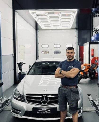 Keys Khammasi – oprichter van KeysCustoms in de werkplaats Keys Khammasi van KeysCustoms poseert voor een Mercedes in de werkplaats